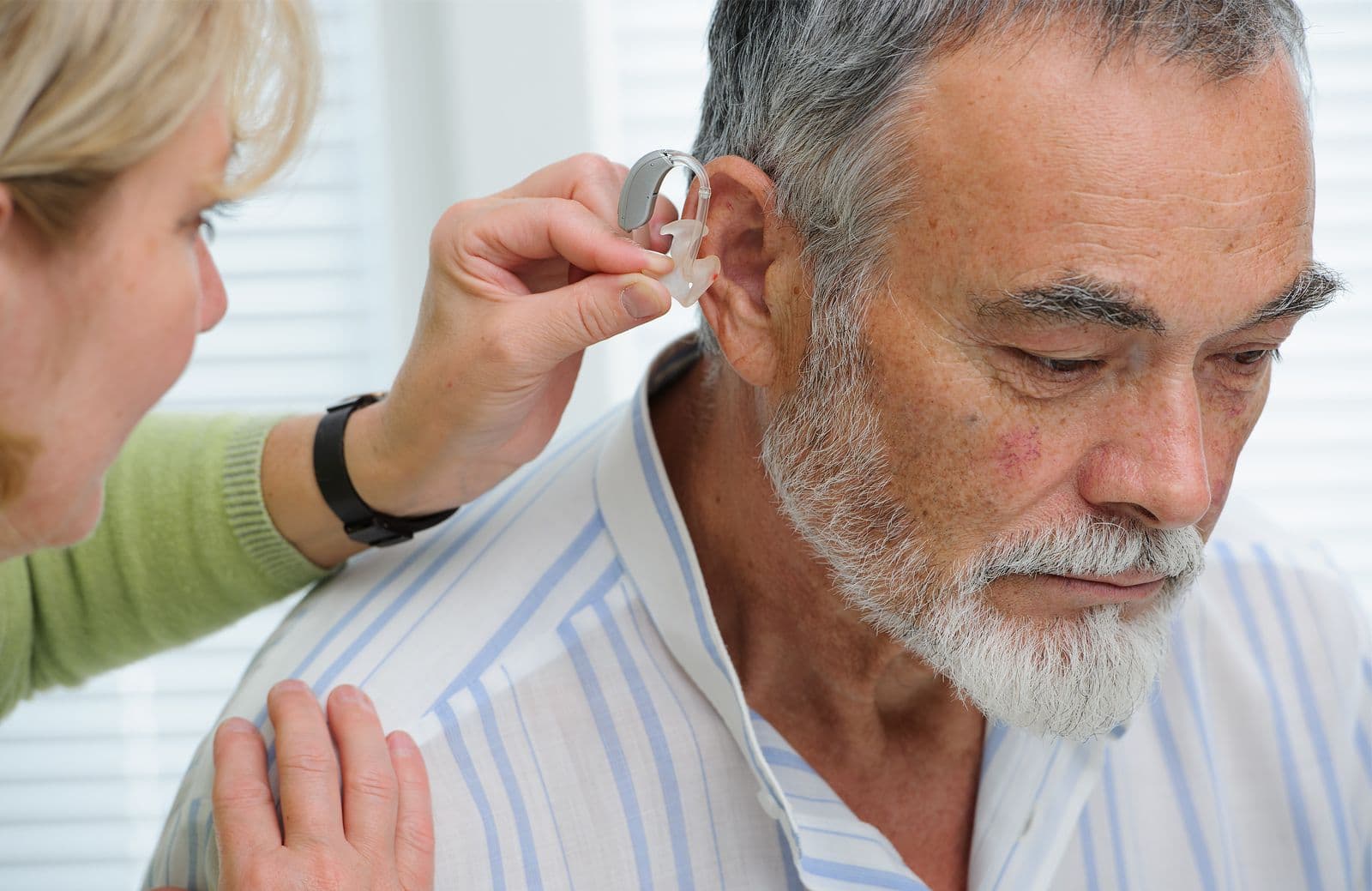 A carer fitting a hearing aid for an older man at home